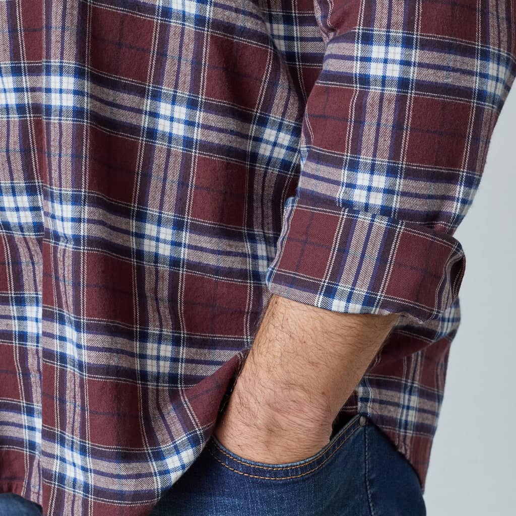 Mann trägt kariertes Hemd mit hochgekrempelten Ärmeln und blaue Jeans in lässiger Pose