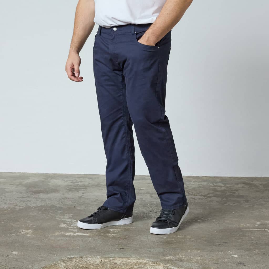 Herren tragen dunkelblaue Hose aus Baumwolle kombiniert mit weißen Sneakern vor hellem Hintergrund