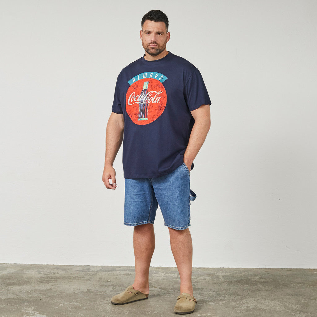 Mann trägt dunkelblaues coca-cola t-shirt mit großem Logo und blauen Jeansshorts