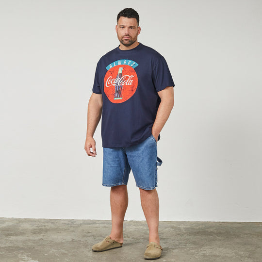 Mann trägt dunkelblaues coca-cola t-shirt mit großem Logo und blauen Jeansshorts