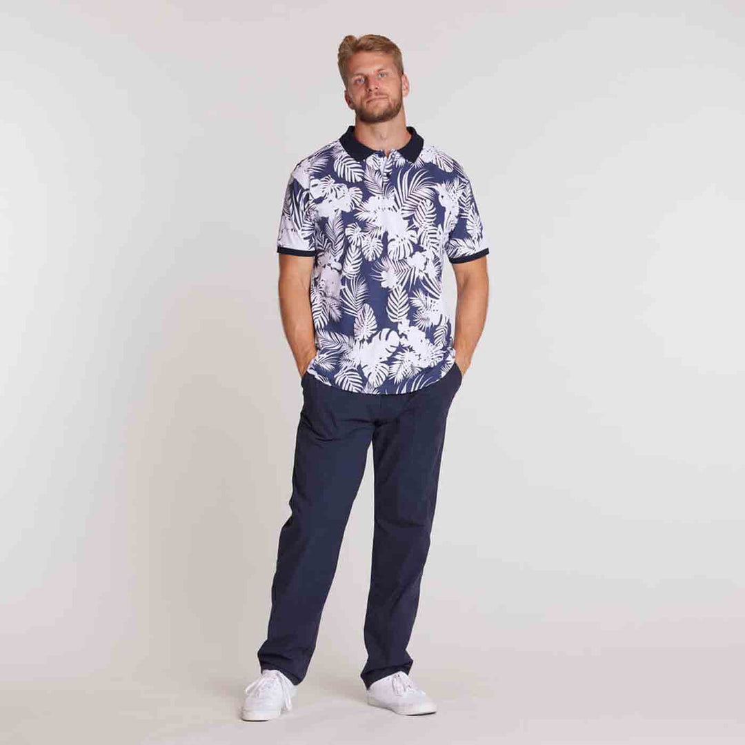 Männliches Modell trägt Allsize Polo Shirt mit weiß-blauem Blattmuster und dunkelblauer Hose