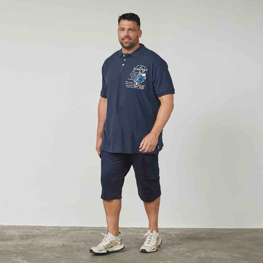 Dunkelblaues polo shirt von Allsize mit Vintage-Motiven getragen von Mann mit Shorts und Sportschuhen