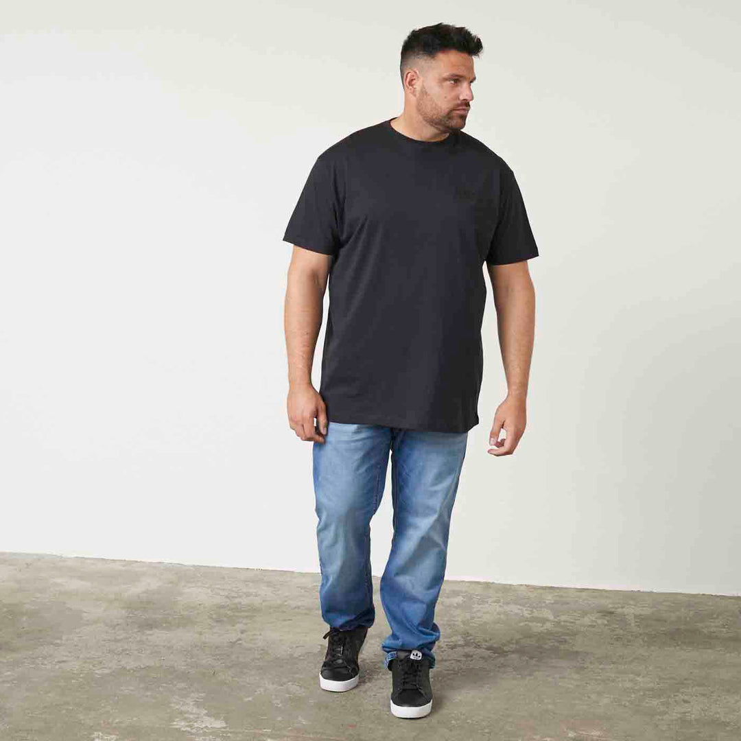 Mann trägt schwarzes t shirt mit druck von Allsize kombiniert mit blauen Jeans und schwarzen Sneakers