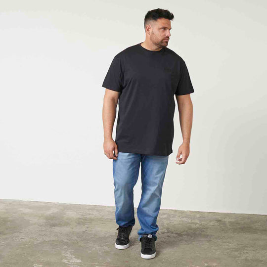 Mann trägt schwarzes t shirt mit druck von Allsize kombiniert mit blauen Jeans und schwarzen Sneakers